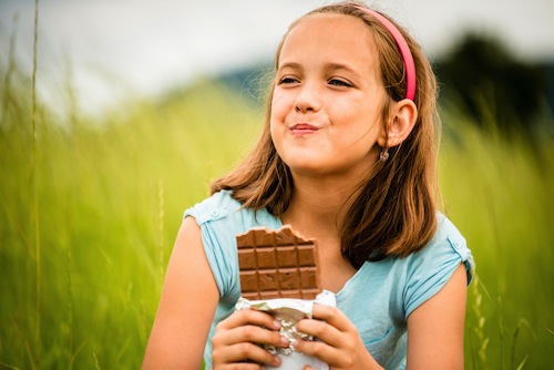 young girl eating and relishing chocolate outdoors