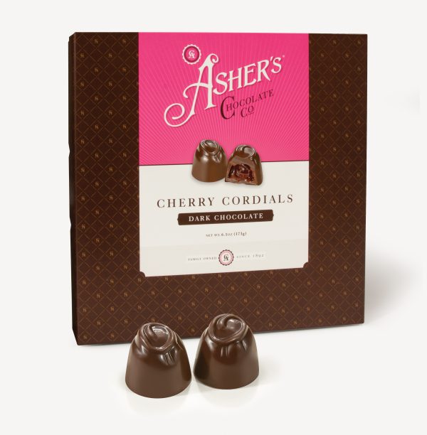 Dark Chocolate Cherry Cordials Traditional Box with pink and white Asher's Chocolate Co. Label. Two (2) Patties on the front of the box reveal, color, size, shape, and texture of candies. Displayed on white background. Two (2) Dark Chocolate Cherry Cordials sit outside of the box to reveal size, color, and chocolate texture.