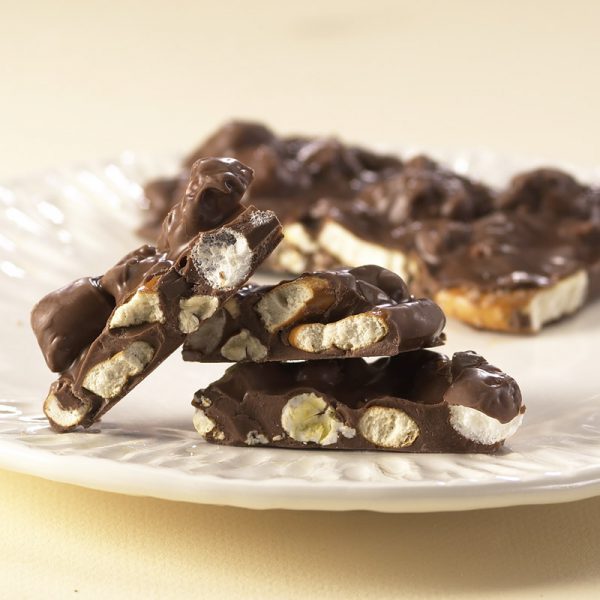 Milk Chocolate Boardwalk Crunch chunks lie on white plate revealing creamy milk chocolate coated popcorn, marshmallows, nuts, and salted pretzels.