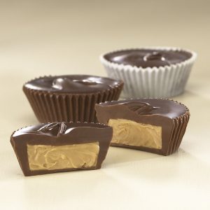 Milk Chocolate Peanut Butter Cups sit on gray background. Two (2) cups are shown whole while two (2) others are cut open to reveal a smooth peanut butter filling.