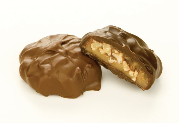 Two (2) Milk Chocolate Pecan Caramel Patties shown on white background. One (1) patty is cut open to reveal caramel and nut filling.