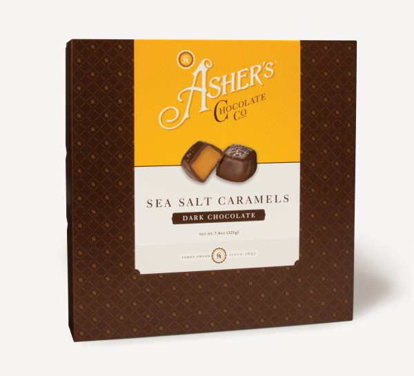 Dark Chocolate Sea Salt Caramels Traditional Box with yellow and white Asher's Chocolate Co. Label. Two (2) caramels on the front of the box reveal, color, size, shape, and texture of candies. Displayed on white background.