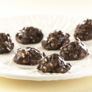 Dark Chocolate Peanut Clusters on white plate. Dark Chocolate chunks are sitting to reveal peanuts coated in globs of dark chocolate.